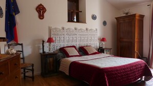 A bedroom with a bed, two bedside tables, a wooden wardrobe, a chair, a dresser, and a wall with decorative panels and a crucifix. - Ferme des Entremains (Thizy-les-Bourgs)