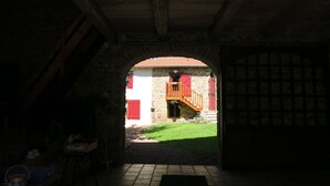 An arched doorway leading to a courtyard with a stone building, a wooden staircase, and a tiled floor. - Ferme des Entremains (Thizy-les-Bourgs)