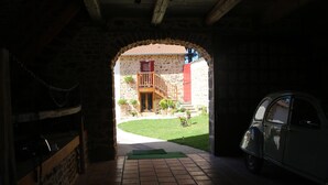 An arched doorway leading to a courtyard with a stone building, a wooden staircase, and a vintage car parked inside. - Ferme des Entremains (Thizy-les-Bourgs)
