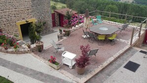 A patio with a table and chairs, surrounded by potted plants and a stone wall. - Ferme des Entremains (Thizy-les-Bourgs)