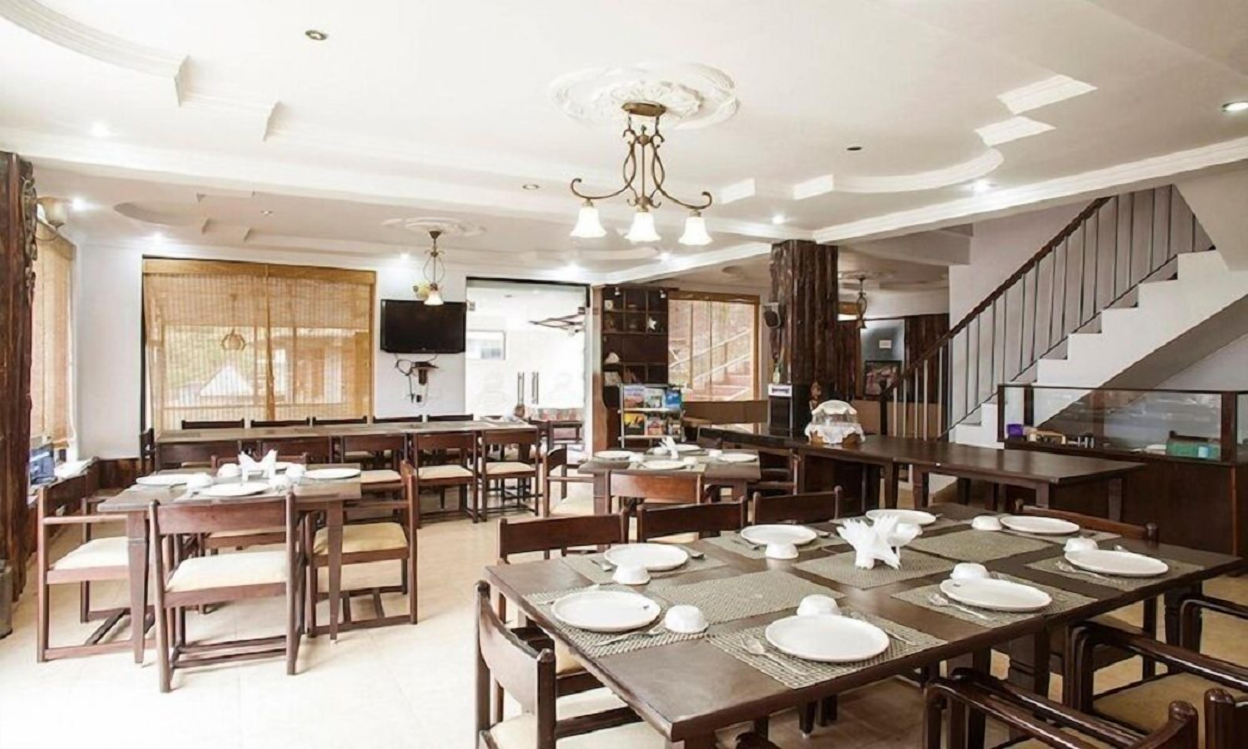 A spacious dining area with multiple tables set for dining, a television mounted on the wall, and a staircase leading to an upper level.