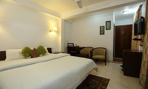 A hotel room with a large bed, a desk, two chairs, a television, and a wardrobe.