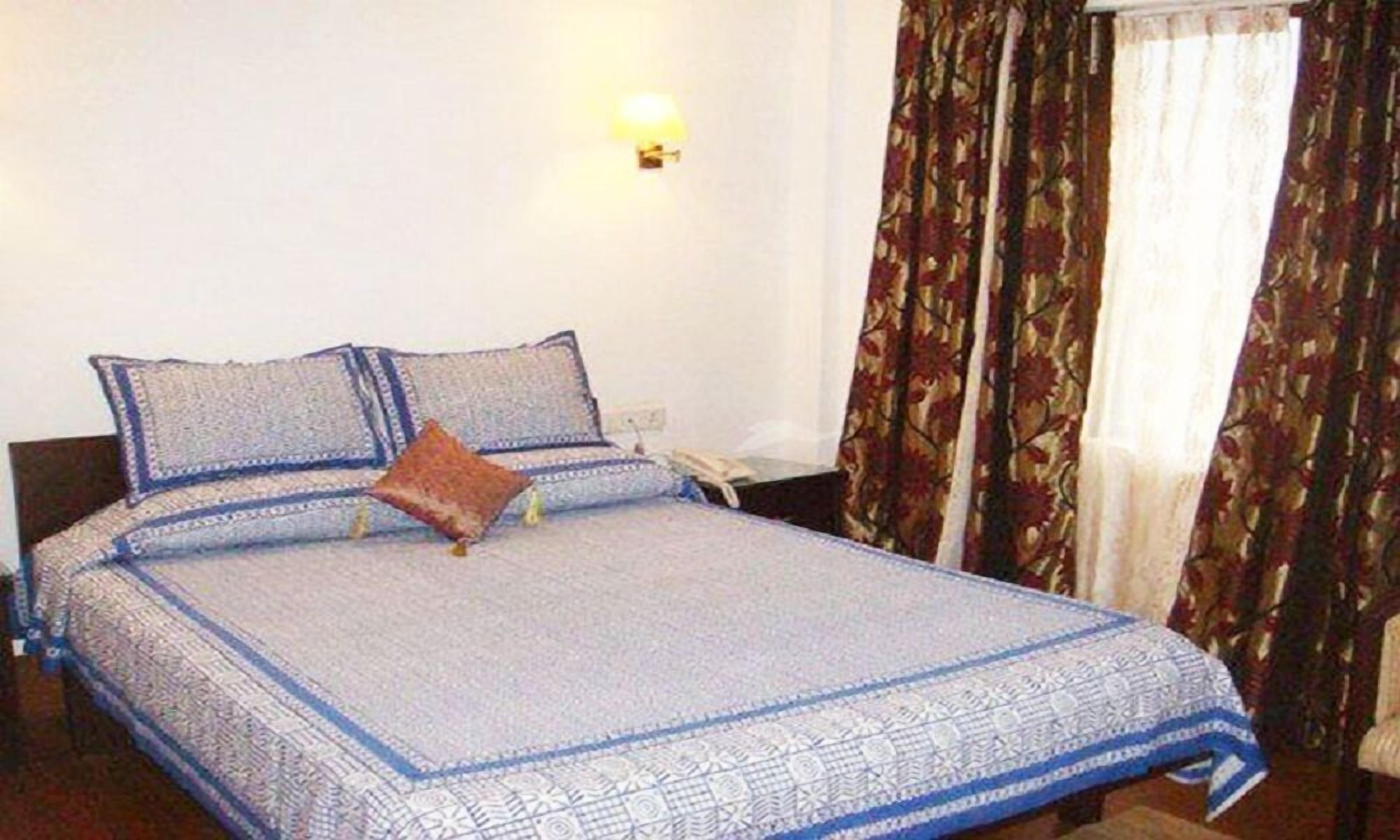A neatly made bed with a patterned bedspread, a pillow, and a bedside table with a lamp.