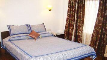 A neatly made bed with a patterned bedspread, a pillow, and a bedside table with a lamp.