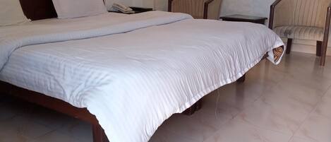 A hotel room with a large bed, two chairs, a nightstand, and a wall-mounted lamp.