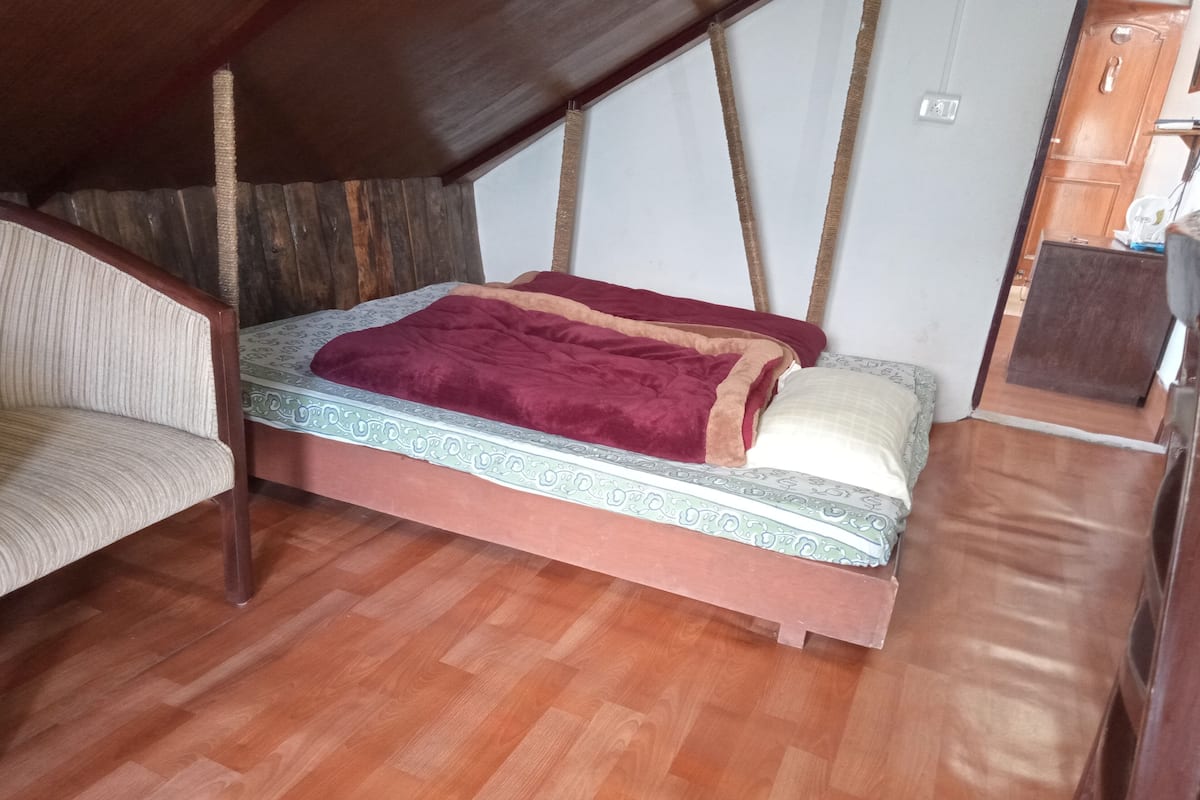 Ein kleiner, gemütlicher Raum mit einem Einzelbett, einem Sessel und Holzdielen.