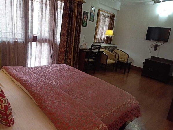 A bedroom with a large bed, a desk, a chair, a television, and a lamp.