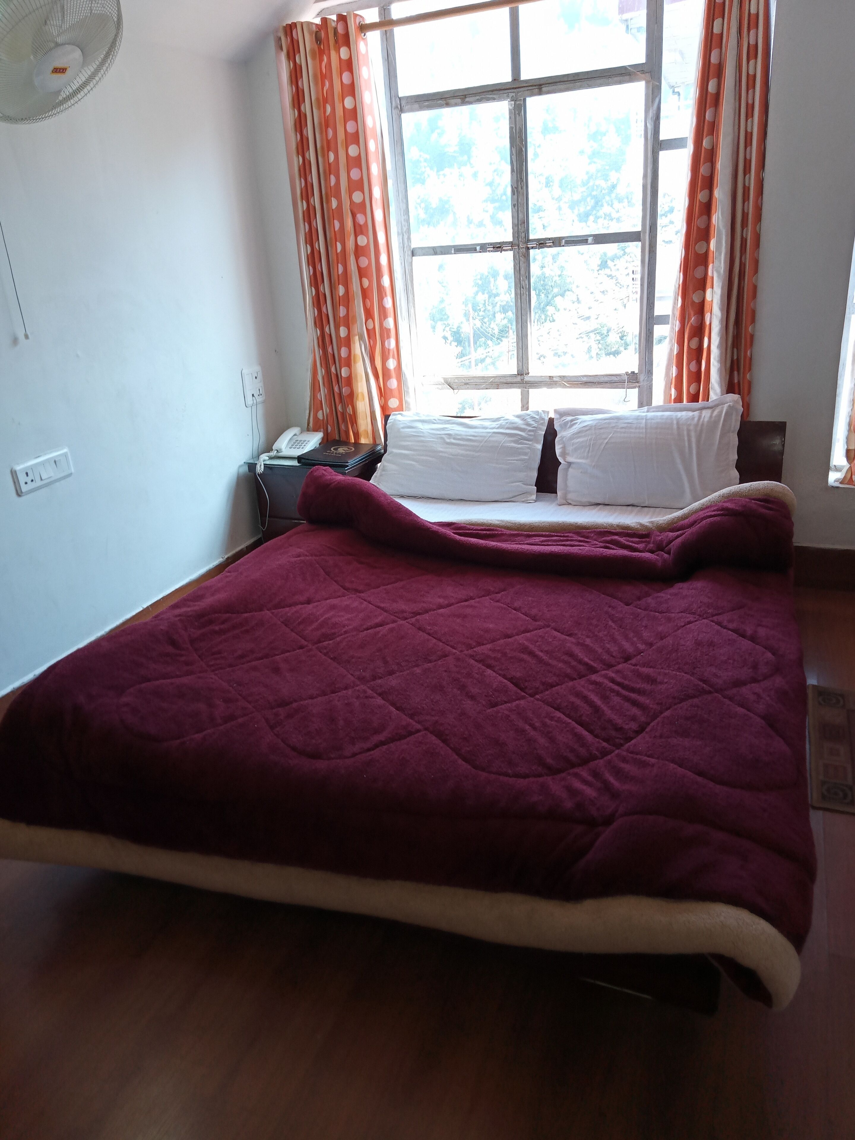 A bedroom with a large bed, a bedside table with a lamp, and a window with curtains.