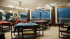 A dining area with tables and chairs, large windows, and a chandelier. - Dragon I Resorts (Dharamshala)