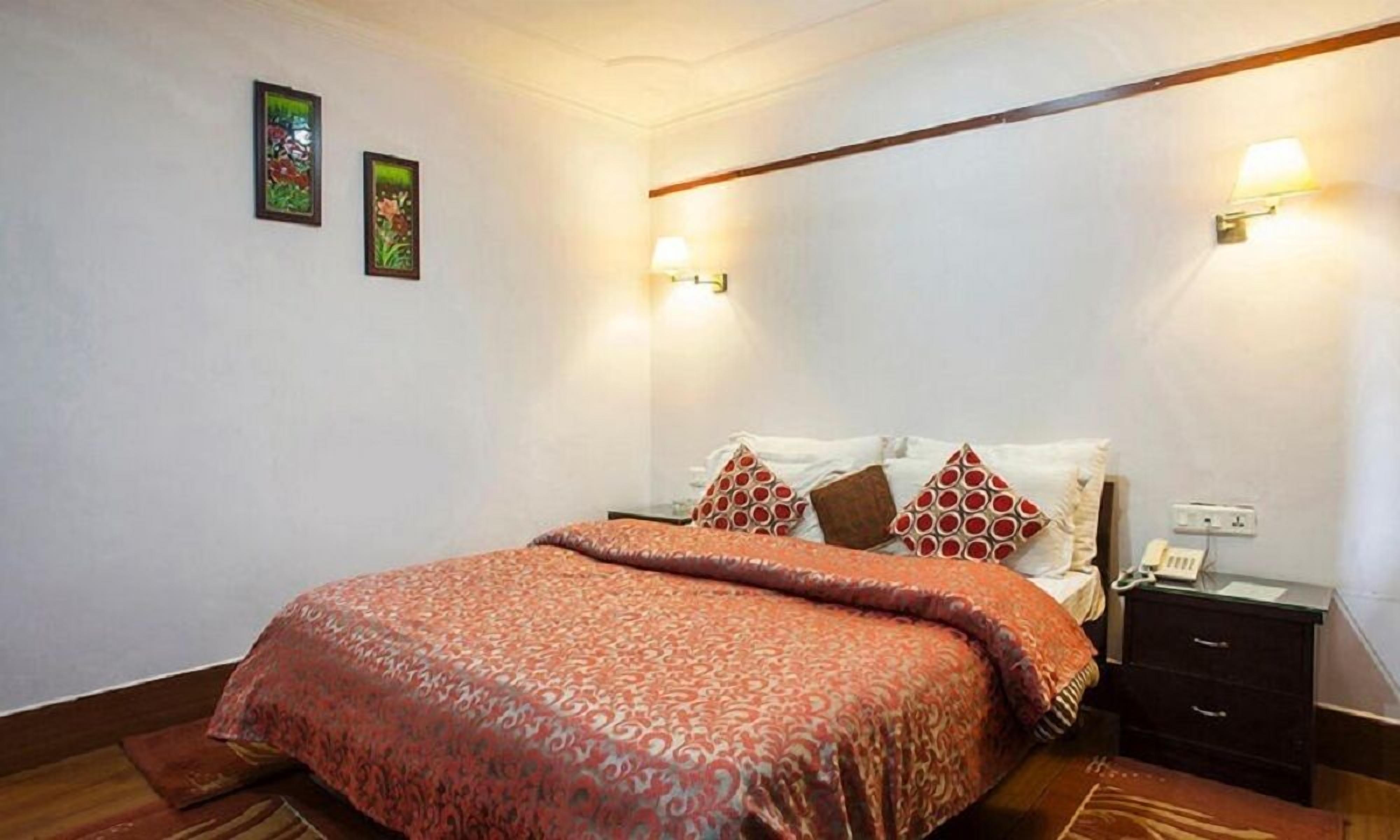 Una cama bien hecha con ropa de cama estampada, una mesita de noche con lámpara y dos apliques de luz en la pared.