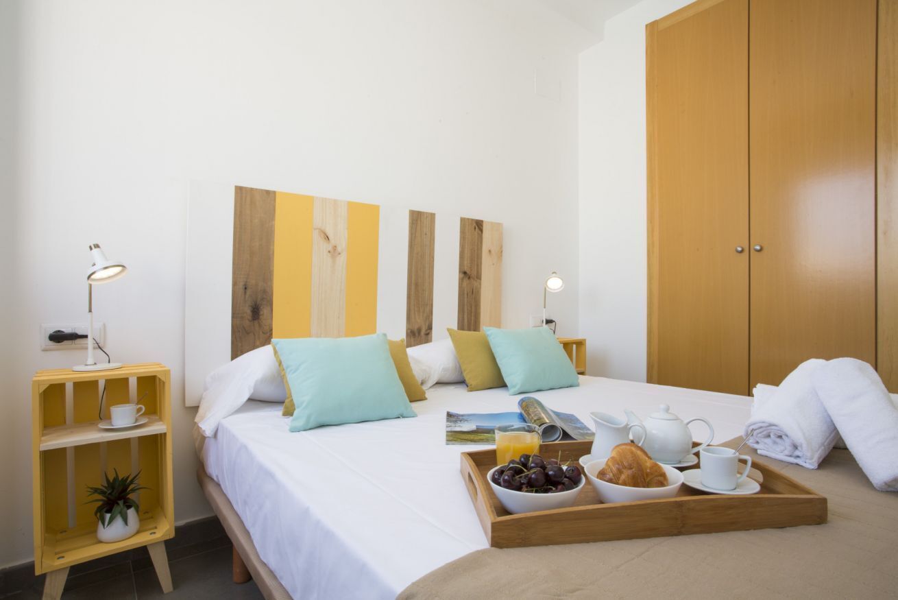 A neatly made bed with pillows, a bedside table with a lamp, a tray with breakfast items, and a wardrobe.