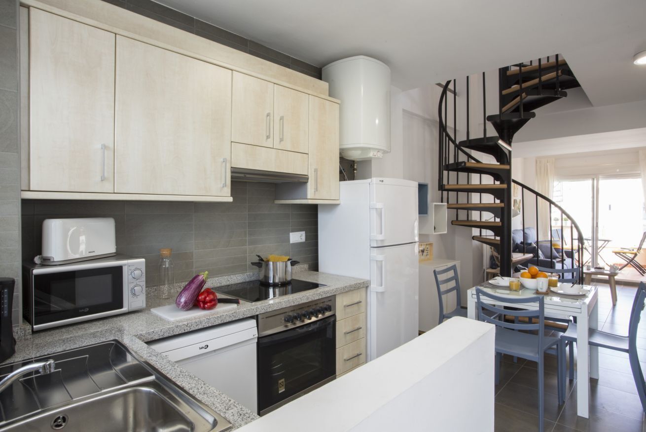 A modern kitchen with a built-in oven, microwave, and sink. A spiral staircase leads to a dining area with a table and chairs.