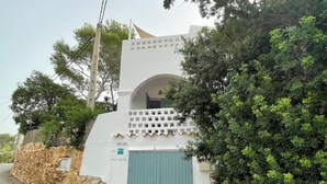 A white building with a blue door, a stone wall, and a green bush. - Charming villa with sea view- next to the beach-Ideal for couples and families (Cala -Vadella)