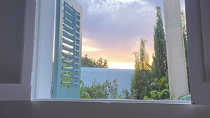 A window with a view of a sunset over the sea, a concrete pillar, and some greenery. - Charming villa with sea view- next to the beach-Ideal for couples and families (Cala -Vadella)