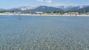 A beach with clear water, mountains in the background, and beach umbrellas. - Hotel Euromar (Massa)