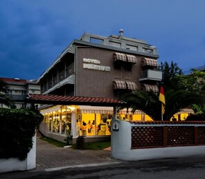 A hotel with a modern facade, large windows, and a balcony with striped awnings.