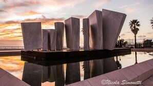 A modern sculpture installation by Nicola Simonetti, featuring geometric shapes and reflective surfaces, set against a sunset backdrop. - Hotel Euromar (Massa)