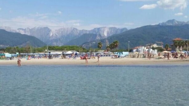 A beach with clear water, mountains in the background, and people on the shore. - Hotel Euromar (Massa)