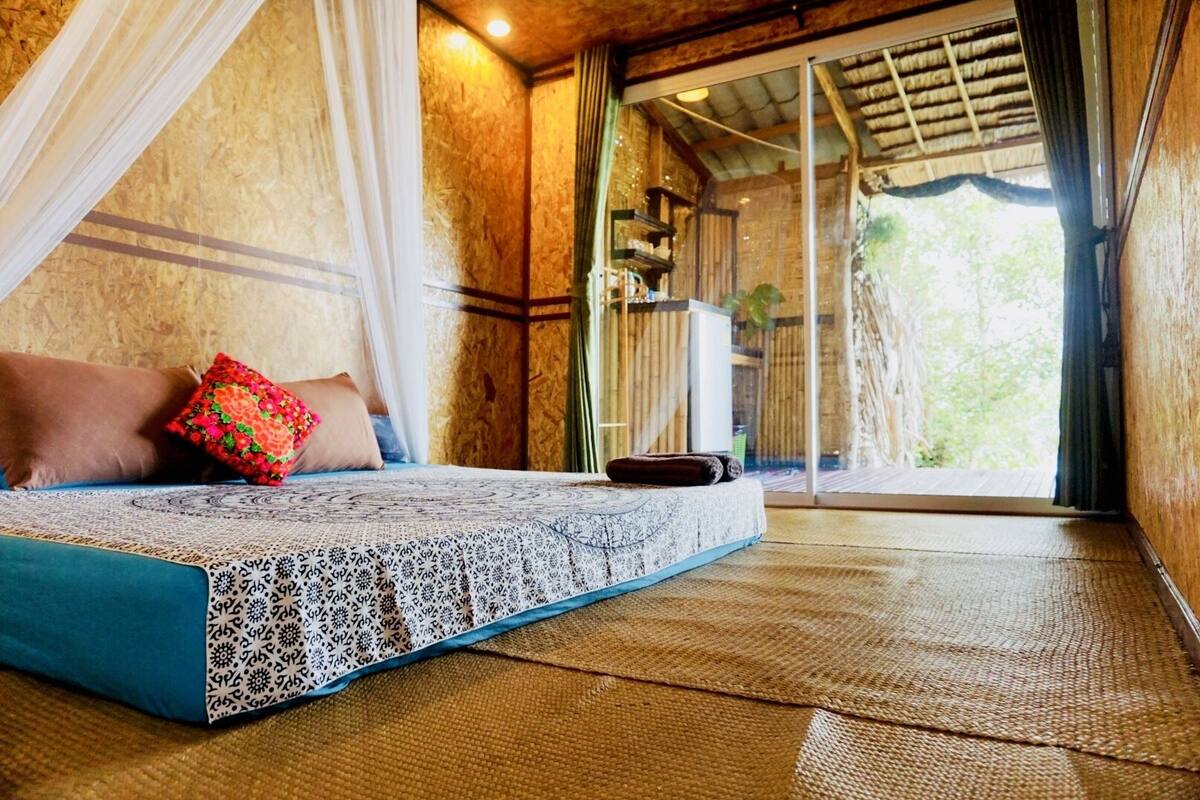 A room with a bed, a window, and a view of greenery outside.