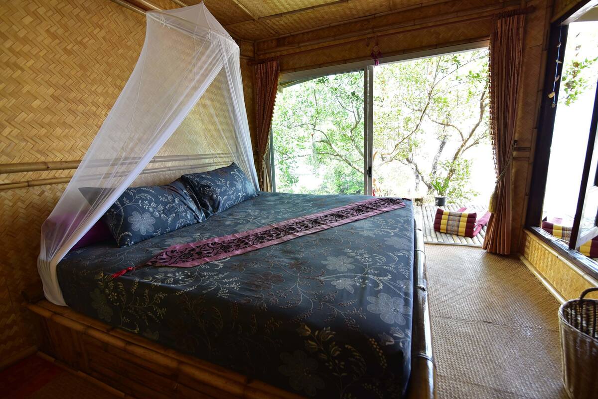A bed with a canopy, a view of trees outside, and a wicker basket.