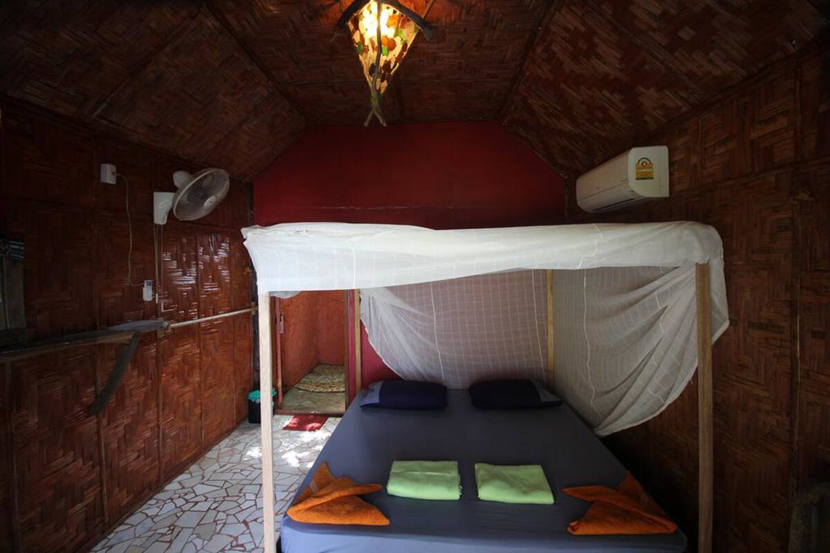 Una habitación con una cama bajo una mosquitera, pared roja, techo de madera y un ventilador de techo.