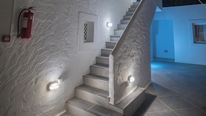 A staircase leading to a white building with a fire extinguisher and lights on the wall. - CALLIOPE MAILLE STUDIOS & APARTMENTS (Kalymnos)