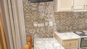 A kitchen with a dining table, chairs, a TV mounted on the wall, and cabinets. - CALLIOPE MAILLE STUDIOS & APARTMENTS (Kalymnos)