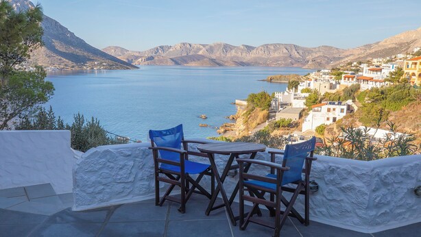 A terrace with a table and chairs overlooking a coastal village and a large body of water. - CALLIOPE MAILLE STUDIOS & APARTMENTS (Kalymnos)