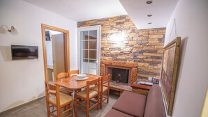 A dining area with a wooden table and chairs, a fireplace, and a television mounted on the wall. - CALLIOPE MAILLE STUDIOS & APARTMENTS (Kalymnos)