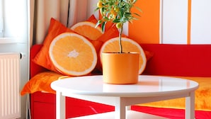 A modern living room with a white round table, a potted plant, and a sofa with orange cushions and a large orange slice.