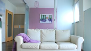 A modern living room with a white sofa, a purple throw blanket, and a wall-mounted art piece.