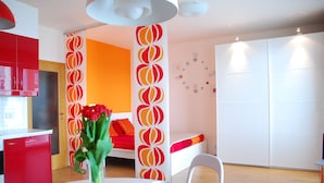 A modern room with a white table, a vase with flowers, a red cabinet, and a white sofa with orange cushions.