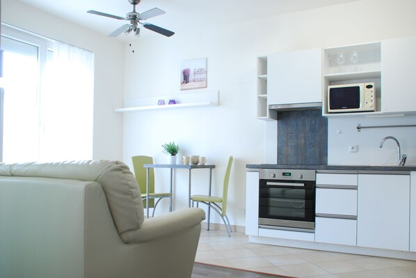 A modern kitchen with white cabinets, a built-in microwave, and an oven. There is a dining area with a table and chairs. - A nice place to stay (Prague)