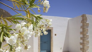 A white building with a blue door, a stone staircase, and white flowers in the foreground.