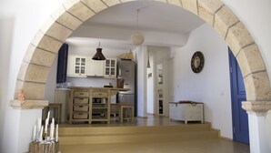 An interior with a stone archway leading to a kitchen area with wooden cabinets and a dining table.