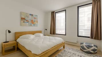Un dormitorio con cama de madera, mesita de noche, lámpara de pie, alfombra estampada y ventana con cortinas.