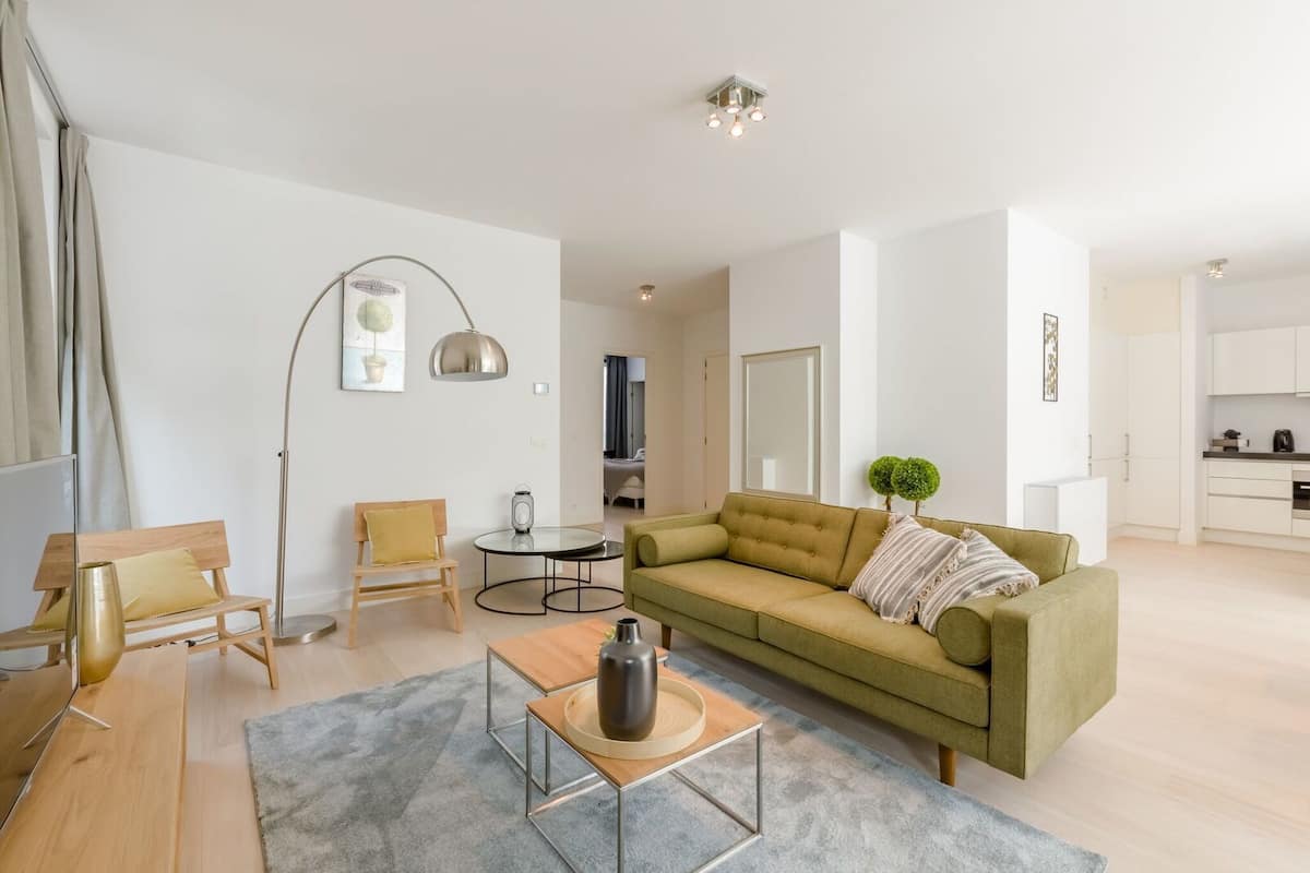 Una sala de estar moderna con un sofá verde, una mesa de centro de madera, una lámpara de pie y una pequeña mesa redonda.