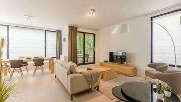 A modern living room with a sofa, coffee table, TV, and dining area.