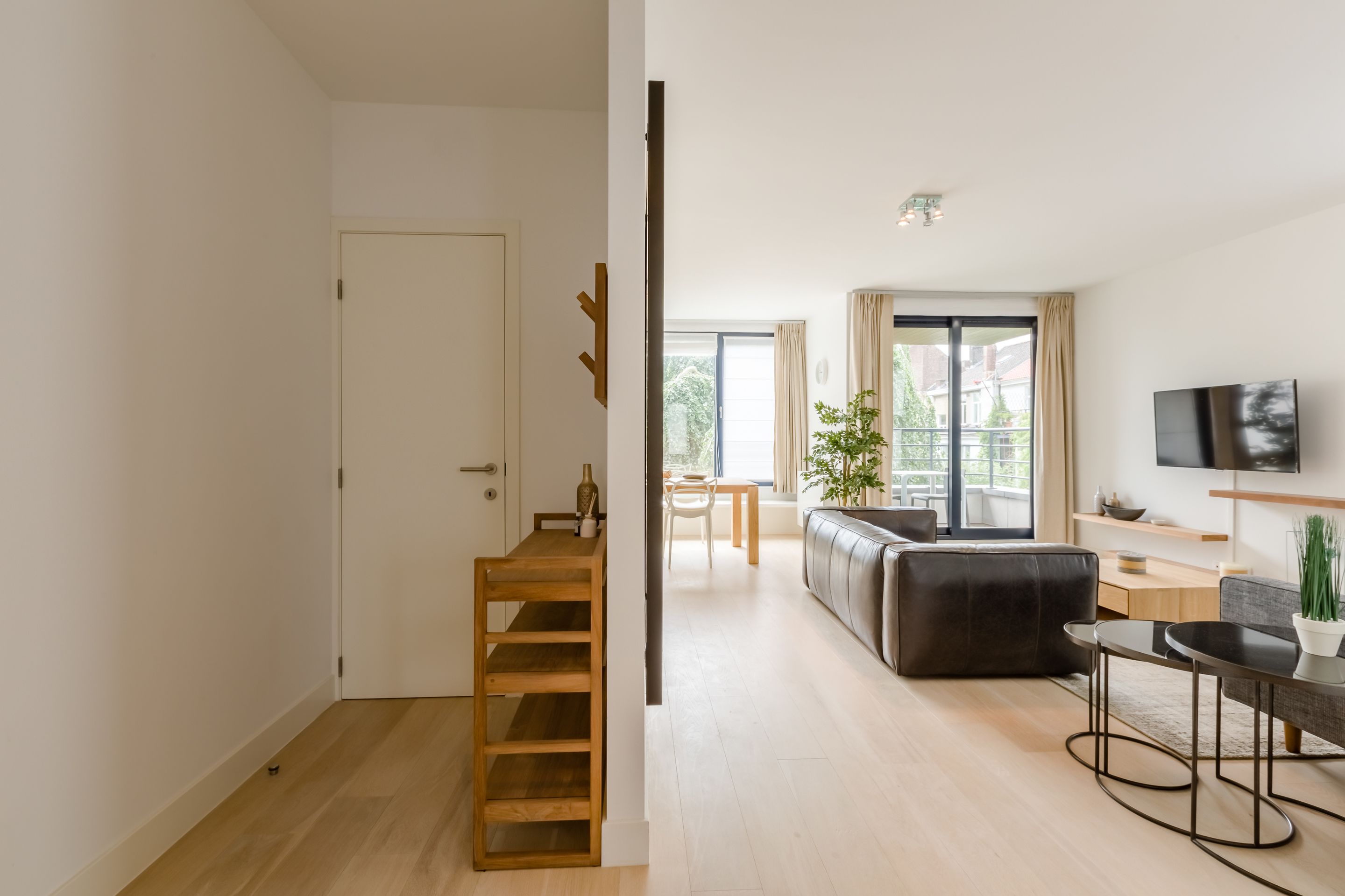 A modern living room with a sofa, a coffee table, and a TV. There is a wooden ladder and a door leading to another room.