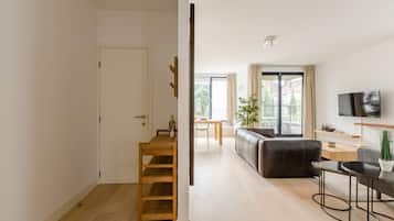 A modern living room with a sofa, a coffee table, and a TV. There is a wooden ladder and a door leading to another room.