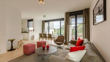 Een moderne woonkamer met een bank, een rode poef, een ronde salontafel en een eethoek met stoelen en een tafel.