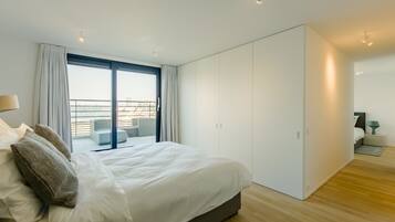 Une chambre moderne avec un grand lit, un placard à portes coulissantes et une vue sur la ville grâce à une grande fenêtre.