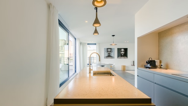 Une cuisine moderne dotée d’un long plan de travail, de luminaires suspendus et offrant une vue sur l’extérieur.