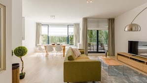 Un salon moderne avec un canapé vert, un coin repas comprenant une table et des chaises, un téléviseur et de grandes fenêtres avec des rideaux.