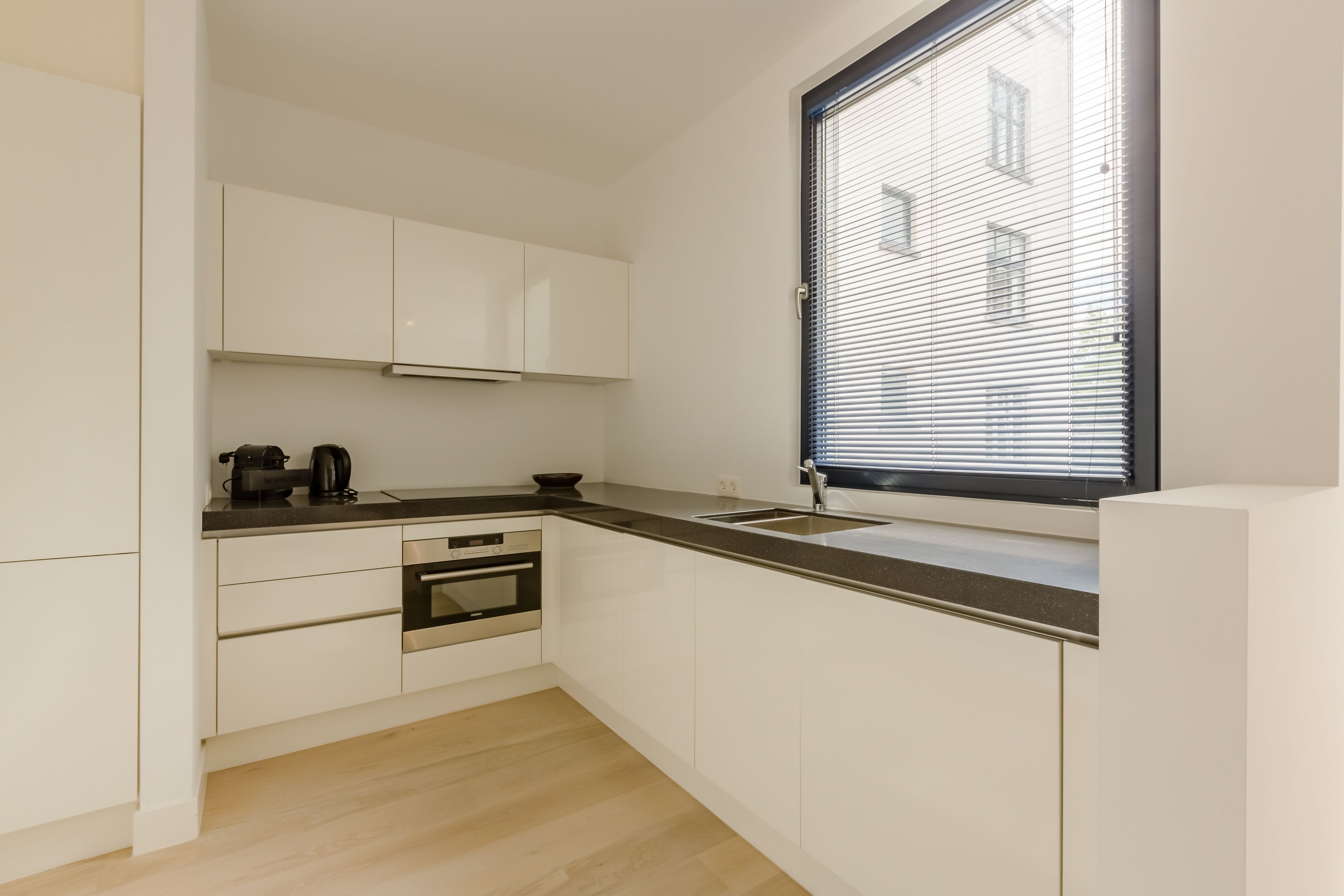 Una cocina moderna con armarios blancos, encimera negra y una ventana con persianas.