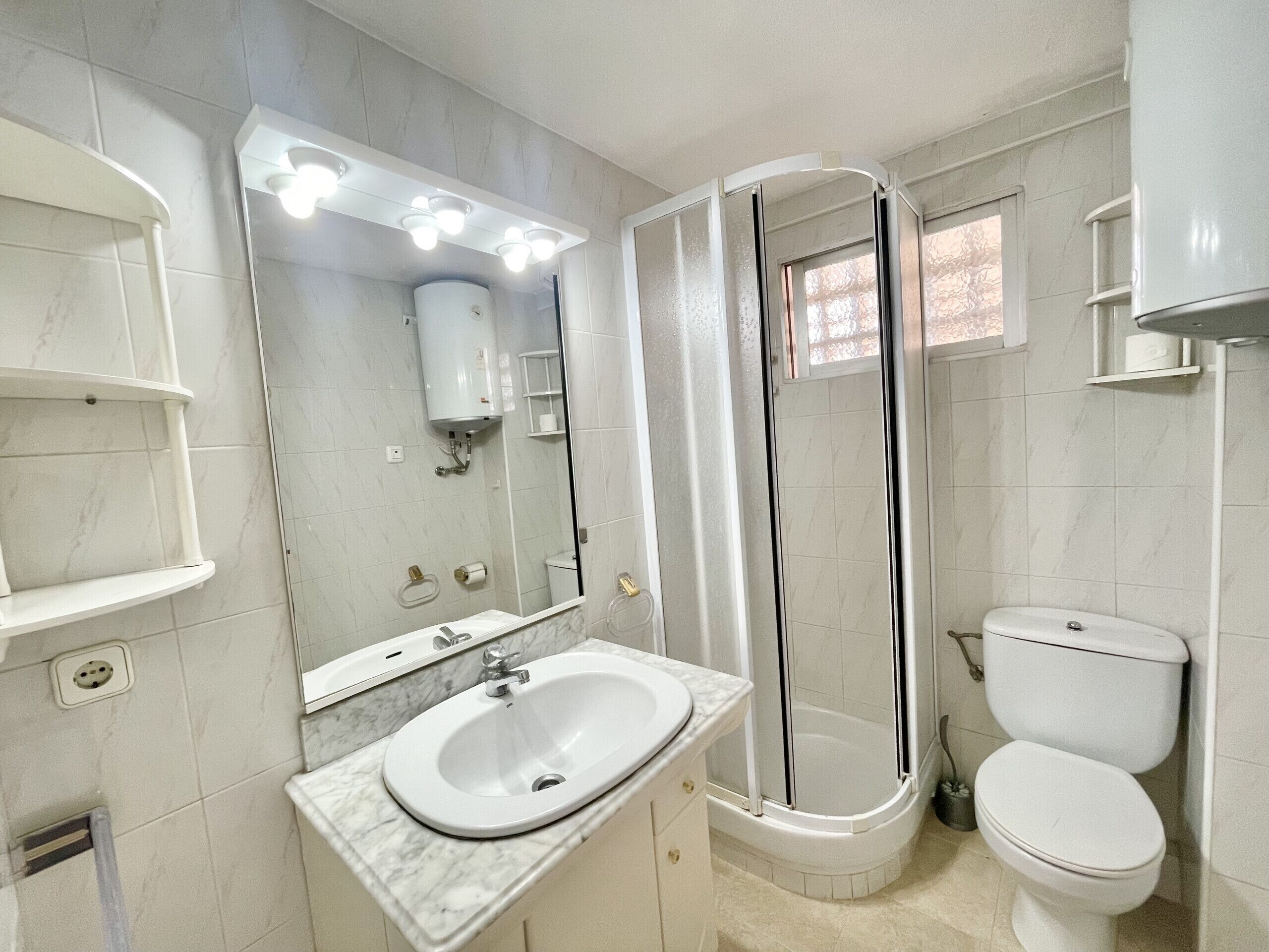 A bathroom with a white sink, mirror, toilet, and shower.