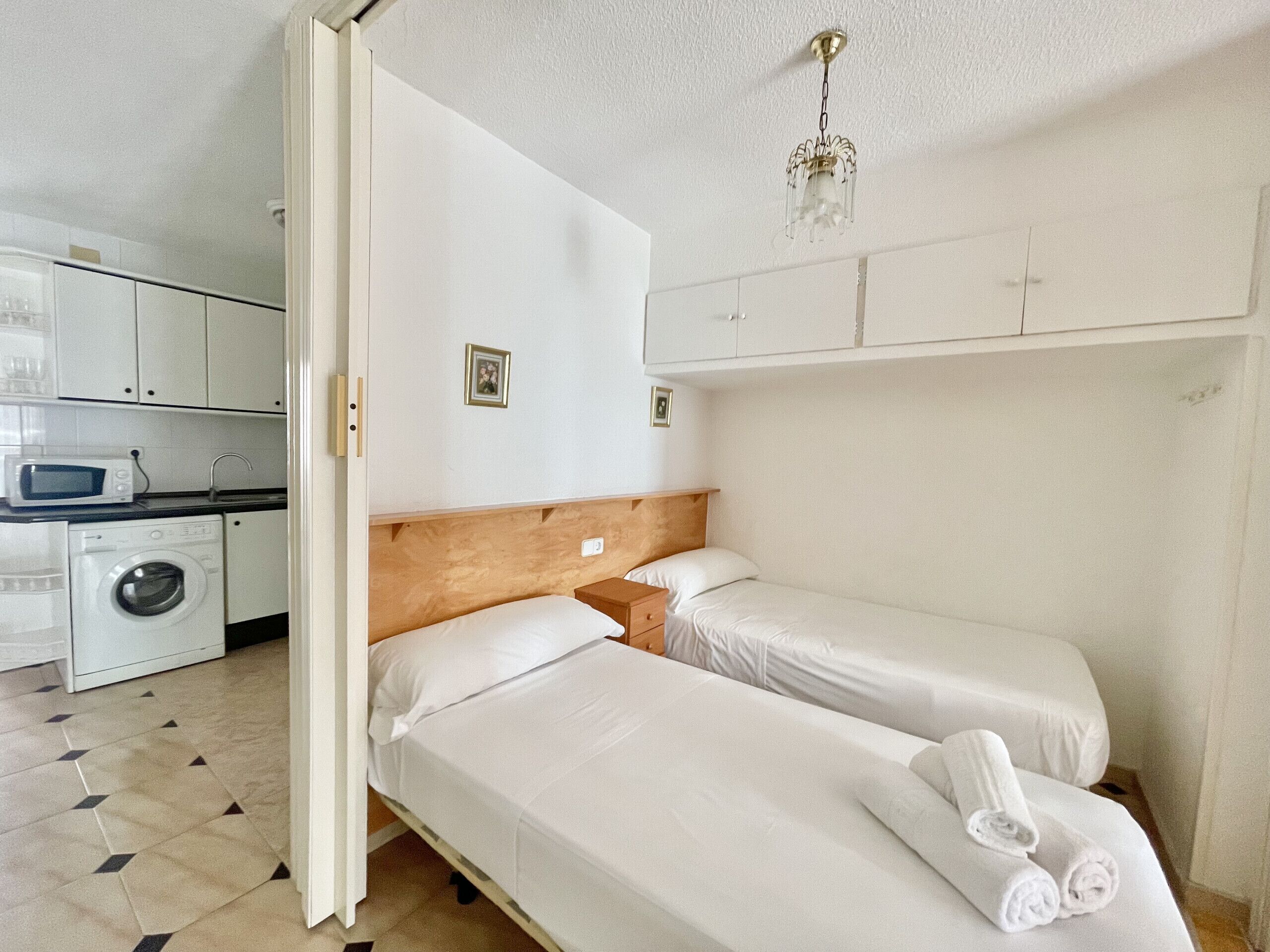 A bedroom with two beds, a wooden headboard, a small bedside table, and a hanging light fixture.