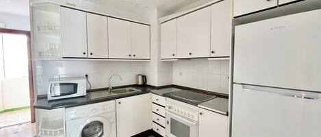 A compact kitchen with white cabinets, a washing machine, a microwave, a sink, and a stove.