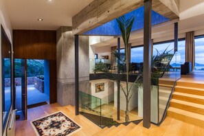 A modern interior with a glass staircase, wooden flooring, and a view of the outdoors.