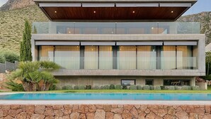 A modern two-story house with a stone facade, large windows, and a swimming pool in the foreground.